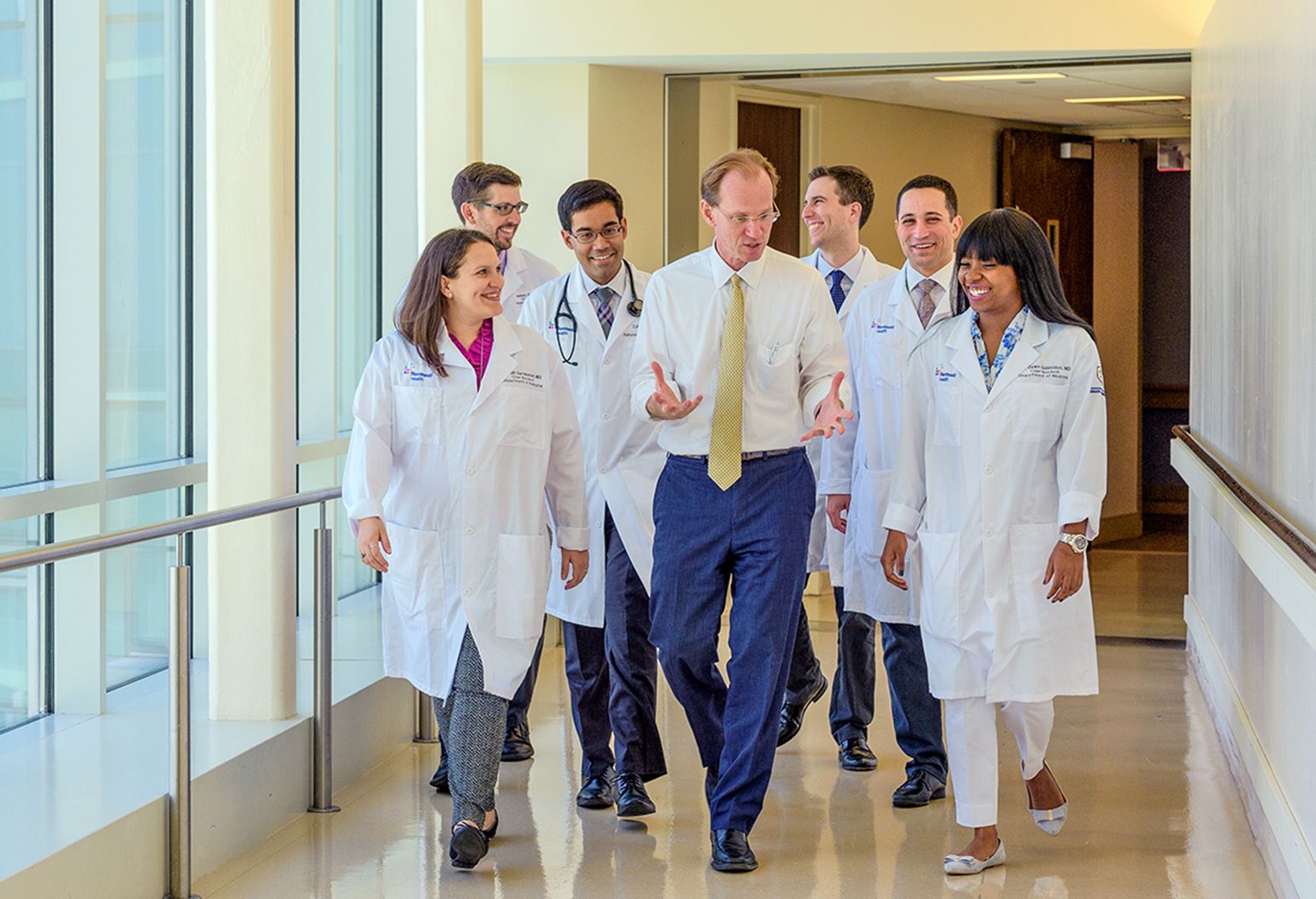 Dr. Thomas McGinn walking and having good conversation with six residents in white lab coats.